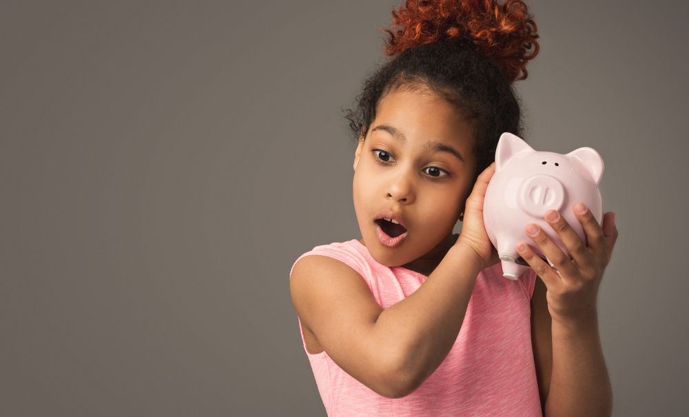 Little black girl with piggy bank, studio shot, copy space